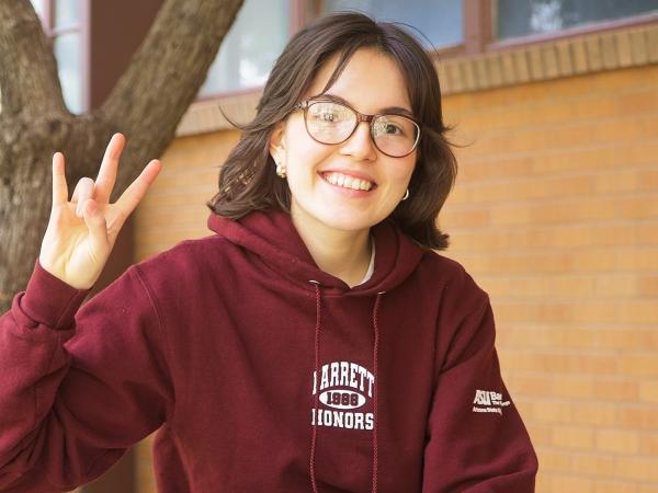 Female student making the pitchfork symbol and smiling at the camera