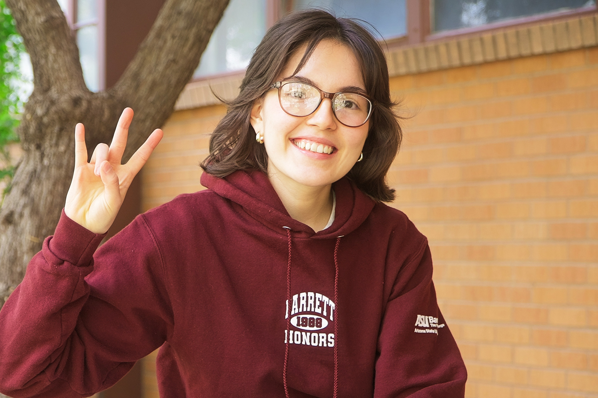 Female student making the pitchfork symbol and smiling at the camera